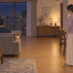 夜のリビングで、スマホを見る夫の背中を見つめる妻